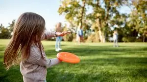 Portrait of happy family of four playing with disc on a green meadow with grass. Focus on daughter. Family, kids and nature concept. Horizontal shot. Rear view