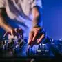 Hands of a male Caucasian DJ playing music on a mixer table in a blue atmosphere. Close up shot.