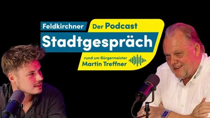 Zwei Menschen sitzen vor einem schwarzen Hintergrund und haben Mikrofone vor sich.