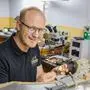 Ein Mann mit Brille sitzt in einer Juwelierwerkstatt und arbeitet an einem Stück