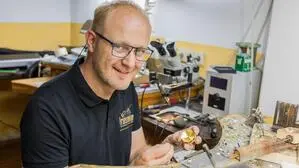 Ein Mann mit Brille sitzt in einer Juwelierwerkstatt und arbeitet an einem Stück