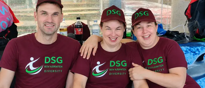 Drei Personen sitzen nebeneinander und tragen die gleiche dunkelrote Uniform mit grüner Schrift und Kappe