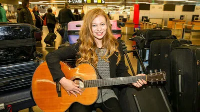 Zoë mit Gitarre zwischen ihren Koffern beim Abflug