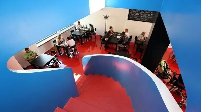 Das Gebäude des Café Era im Stadtteil Černá Pole wurde in den 1930e- Jahren des vergangenen Jahrhunderts im funktionalistischen Stil erbaut. Hier traf sich die Brünner Oberschicht. Im zweistöckigen Café mit Vorgarten fanden ursprünglich 240 Gäste Platz und das Café diente bis zum Jahr 1978 seinem Zweck. Nach vielen Jahrzehnten, in denen das Gebäude verfiel, wurde es nun renoviert und heute können Sie hier erneut Ihren Kaffee genießen. Eine Dominante der Inneneinrichtung ist die Wendeltreppe, die die beiden Stockwerke des Cafés miteinander verbindet. Bestimmt wird Sie auch die Gebäudefront des Cafés begeistern, die an ein Plakat erinnert.