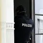 Polizist von hinten, während er gerade durch eine Haustür geht | Die Polizei stellte bei der Hausdurchsuchung mehrere Beweisgegenstände sicher (Symbolfoto)