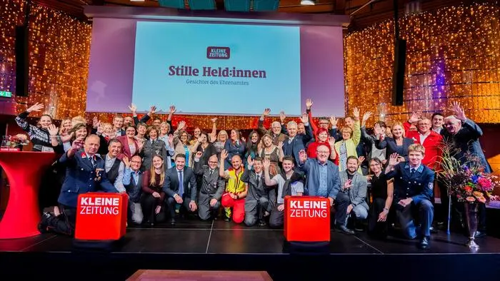Viele Menschen stehen auf einer Bühne und lachen und winken in die Kamera