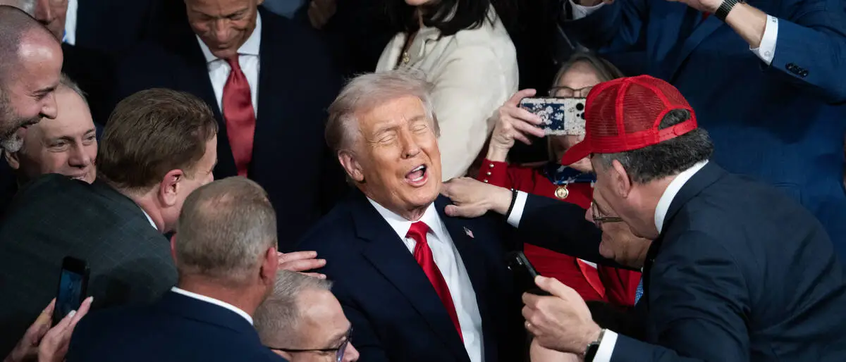 Donald Trump steht inmitten einer dichten Menschenmenge. Mehrere Personen umringen ihn, einige machen Fotos mit ihren Smartphones, während andere ihm die Hand reichen oder ihn berühren. | Trump beschwört „goldenes Zeitalter“