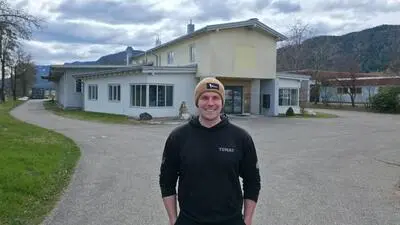 Ein Mann mit Haube steht vor einem Gebäude, um das die Straße links und rechts herumführt