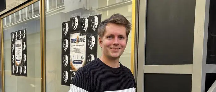 Ein Mann steht vor einem Geschäft, im Hintergrund sieht man Plakate mit der Ankündigung