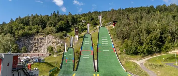 Drei Sprungschanzen im Sommer, gesäumt von vielen Bäumen