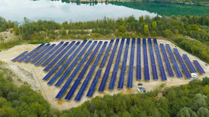 Luftbild PV-Anlage auf Schotterfläche, dahinter Stausee