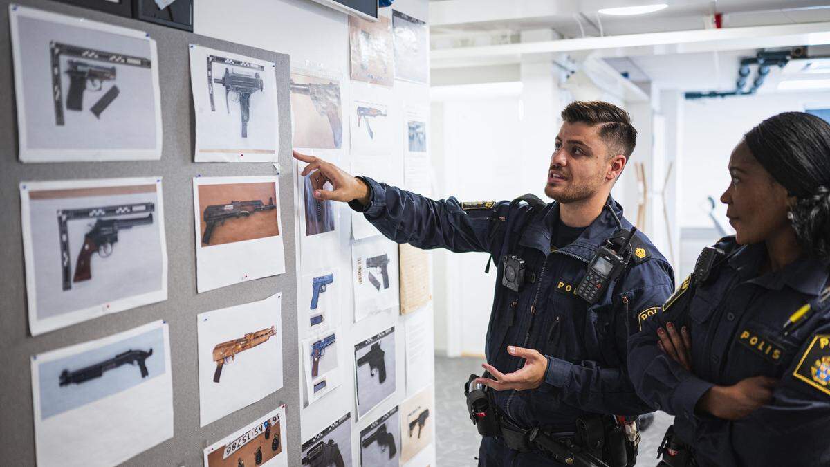 Ein Polizist und eine Polizistin inspizieren Fotos beschlagnahmter Waffen im Wachzimmer in Rinkeby 