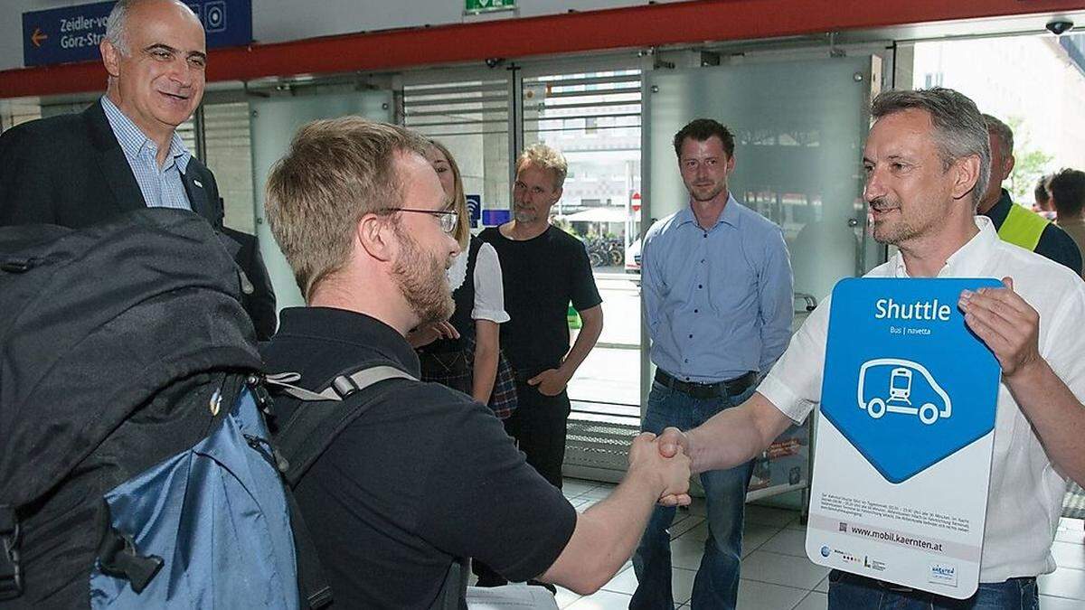 Regions-Geschäftsführer Georg Overs (links) und Reinhard Schildberger, Mobilitätscoach von Südkärnten begrüßen die ersten Bahnhof-Shuttle-Nutzer in der Ankunftshalle des Villacher Hauptbahnhofes