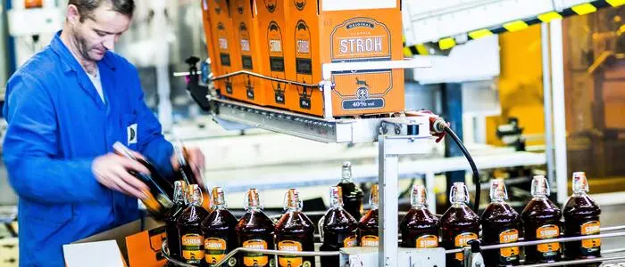 Zu sehen ist ein Mitarbeiter, der in der Produktion Flaschen der Marke Stroh in einen Karton einsortiert | Die Nachnutzung des Stroh-Werks in der Strohgasse im Süden von Klagenfurt ist noch offen