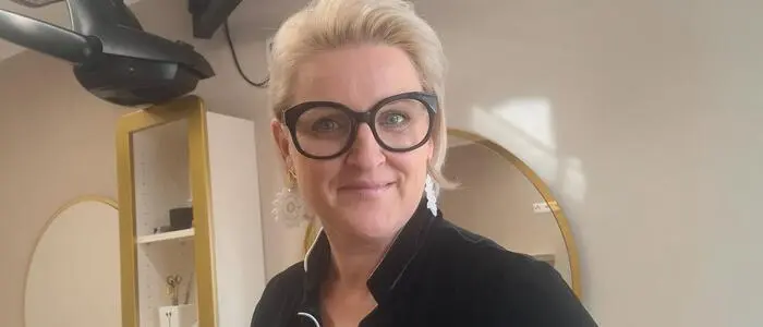 Eine blonde Dame lächelt in einem Friseursalon in die Kamera