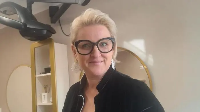 Eine blonde Dame lächelt in einem Friseursalon in die Kamera