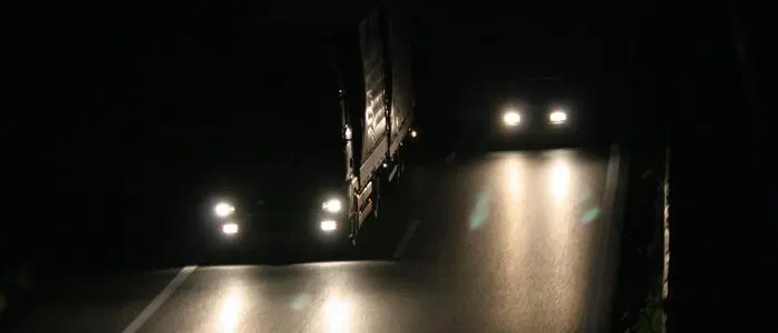 Das Bild zeigt einen LKW, der neben einem PKW bei Dunkelheit auf der Autobahn fährt