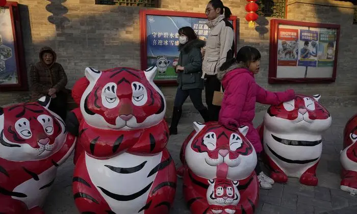 Residents pass by Chinese New Year decorations along an alley way in Beijing, China, Tuesday, Jan. 11, 2022. The Chinese capital is on high alert ahead of the Winter Olympics as China locks down a third city elsewhere for COVID-19 outbreak. (AP Photo/Ng Han Guan)