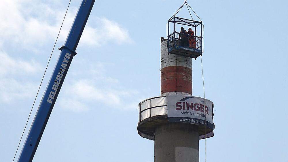 In mehr als 50 Metern Höhe tragen Bauarbeiter die Kaminspitze ab