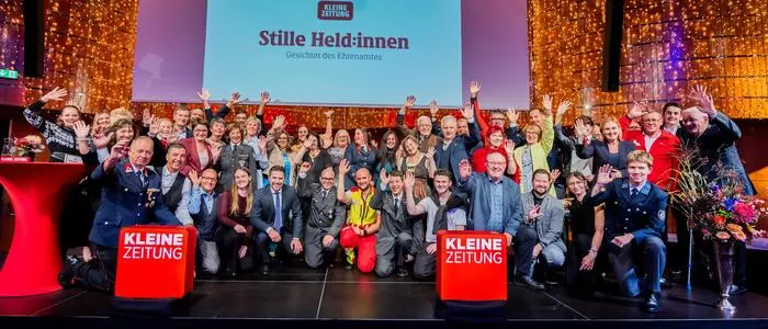 Viele Menschen stehen auf einer Bühne und lachen und winken in die Kamera