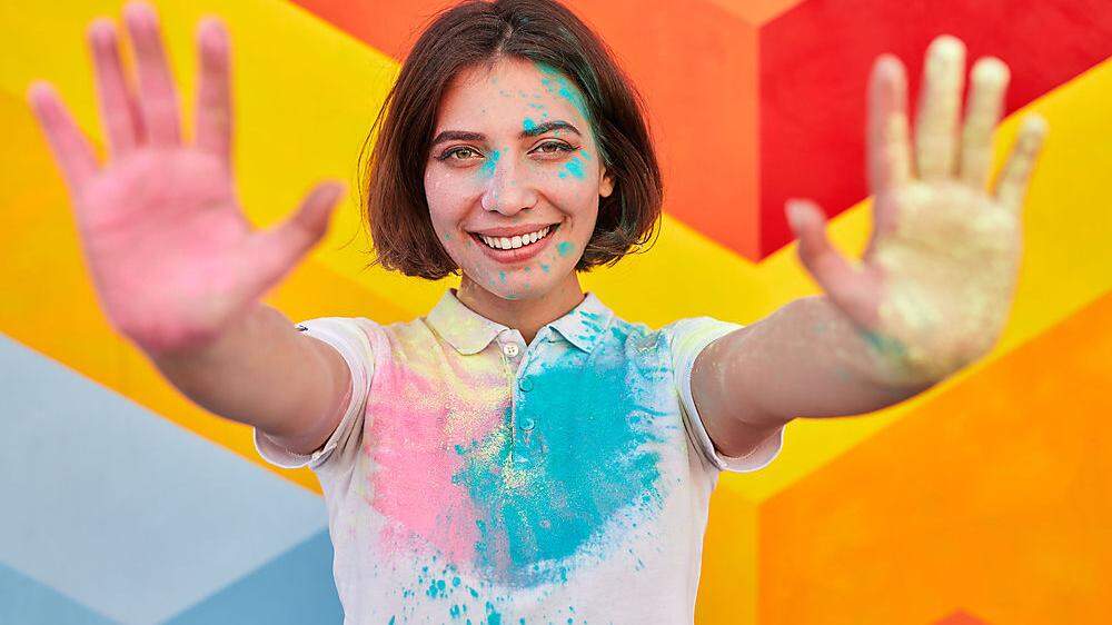 Happy woman with colorful face and clothes showing hands