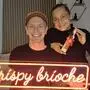 Ein Mann und eine Frau lächeln in die Kamera. Der Mann hält ein Leuchtschild mit der Aufschrift „Crispy Brioche“ vor der Brust. | Manuela Dunkel und Florian Detlefsen gründeten gemeinsam „Crispy Brioche“