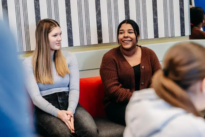 Stella-Marie Harry, langes offenes Haar, und Dijana Zejnullahu, mit zusammengebundenen dunklen Haaren, sitzen auf einer Bank in der Schule