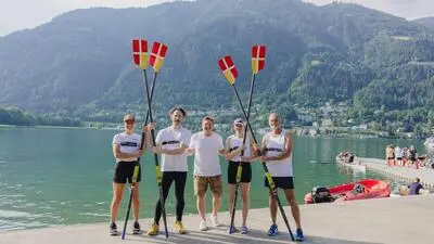 Mehrere Ruderinnen und Ruderer stehen mit Paddeln vor einem See