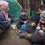 A family rests at a camp set up by migrants near the Belarusian-Polish border in the Grodno region on November 13, 2021. - Thousands of migrants -- most of them from the Middle East -- have crossed or attempted to cross the EU and NATO border since the summer. Western countries have accused the Belarusian regime, which is backed by Russia, of engineering the crisis in retaliation against EU sanctions, charges that Minsk has denied. (Photo by Leonid SHCHEGLOV / BELTA / AFP) / Belarus OUT