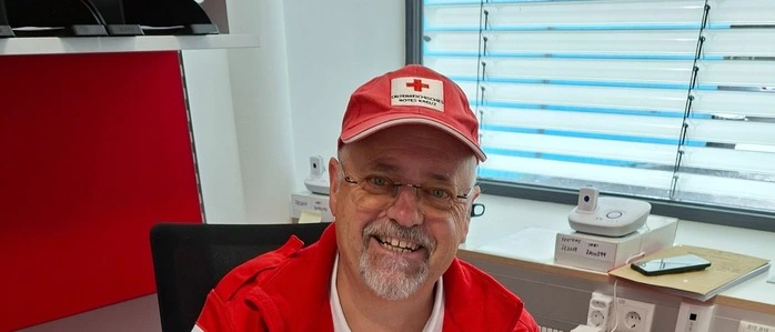 Ein Mann in einer Rot-Kreuz-Uniform hält einen Katalog für Betreutes Reisen in die Kamera
