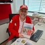 Ein Mann in einer Rot-Kreuz-Uniform hält einen Katalog für Betreutes Reisen in die Kamera