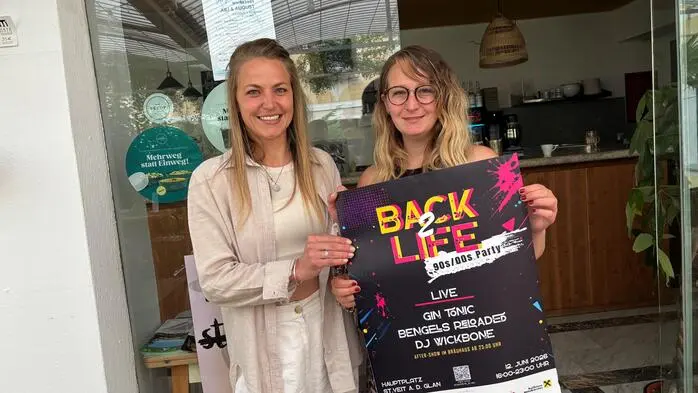 Zwei blonde Frauen halten ein Plakat in die Kamera