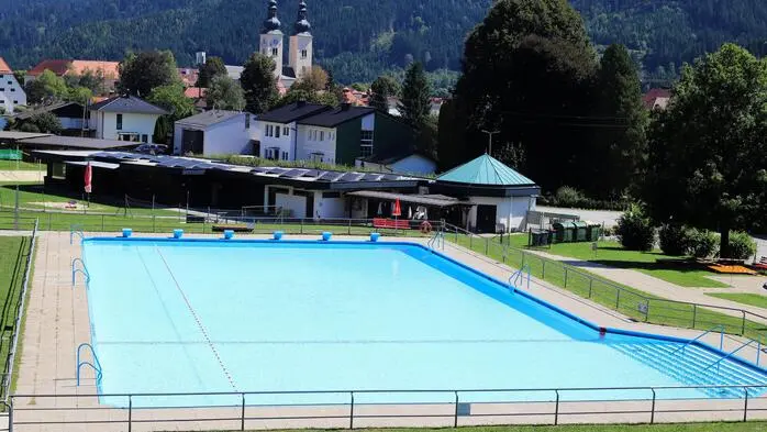 Ein Becken in einem Freibad. Dahinter die Ortschaft Gurk mit dem Gurker Dom 