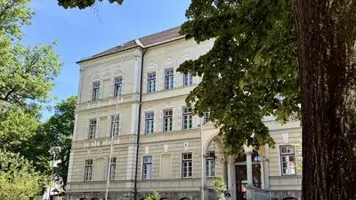Seitlicher Blick auf ein altes Gebäude. Im Vordergrund sieht man einen Baum