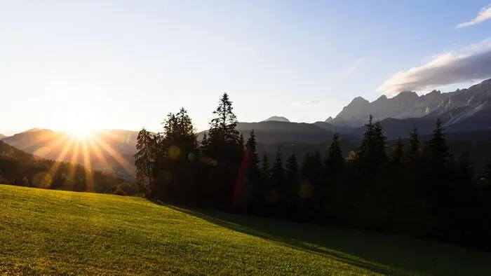 Die Sonne geht über einem Bergkamm am Horizont unter und scheint auf eine grüne Alm irgendwo in der Steiermark