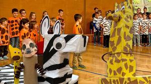 Rund 100 Volksschülerinnen und - schüler werden mit Giraffe, Zebra, Erdmännchen und Löwe auf der Bühne stehen