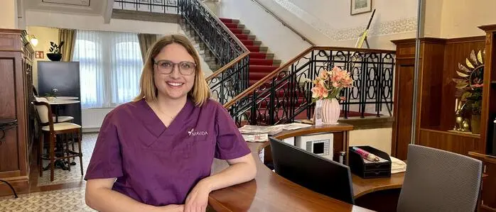 Eine junge Frau in Pflegekleidung vor einer Rezeption 