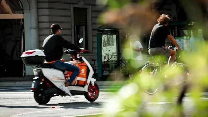 Ein Essenszusteller fährt auf seinem E-Moped auf einem Radweg, vor ihm ist ein Radfahrer unterwegs
