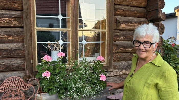 Eine Dame mit weißen Haaren und Brille steht neben einem Blumenstock