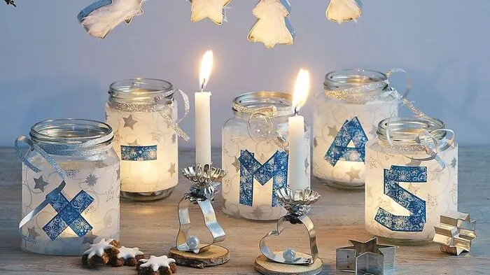 Man braucht: 5 Schraubgläser (ca. 7 cm Ø, 11 cm hoch), gemustertes Transparentpapier, Deko-Tape (15 mm breit), silbernes Geschenkband zum Kräuseln, Teelichter oder kleine Stumpenkerzen Für die Weihnachtsgläser jeweils eine Manschette aus Transparentpapier zuschneiden, dabei den jeweiligen Glasumfang und die Glashöhe beachten. Mit dem Deko-Tape mittig auf jeder Manschette einen Buchstaben für das Wort „XMAS“ gestalten. Dann die Manschetten um die Gläser legen und mit Klebefilm fixieren.