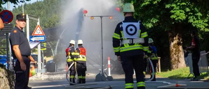 Mehrere Feuerwehrmänner machen eine Übung, löschen mit Wasser, das aus einem Schlauch kommt.