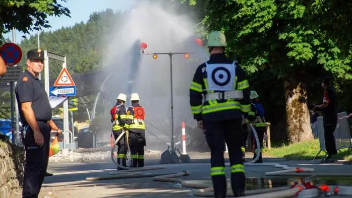 Mehrere Feuerwehrmänner machen eine Übung, löschen mit Wasser, das aus einem Schlauch kommt.