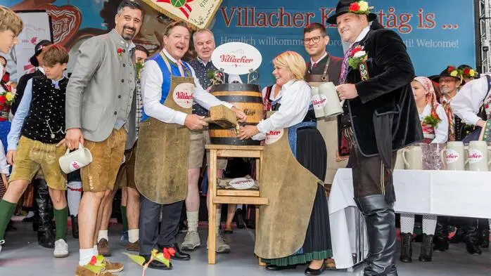 Mehrere Menschen stehen um ein Bierfass, das angestochen wird auf einer Bühne