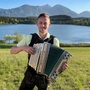 Ein Mann steht mit einer Harmonika vor einem See