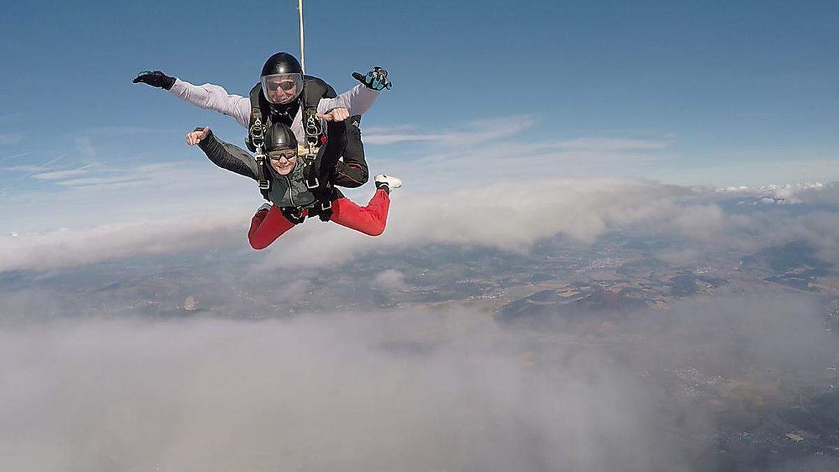 Mit einem Tandemmaster springen Wagemutige beim Fallschirmspringen aus einem Hubschrauber in Richtung Erde  