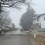 Eine Straße, umgeben von dichtem Nebel, wobei auf einer Seite eine Bushaltestelle und ein Haus zu sehen sind | Gegenüber dieser Haltestelle entsteht nun eine neue