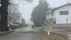 Eine Straße, umgeben von dichtem Nebel, wobei auf einer Seite eine Bushaltestelle und ein Haus zu sehen sind | Gegenüber dieser Haltestelle entsteht nun eine neue