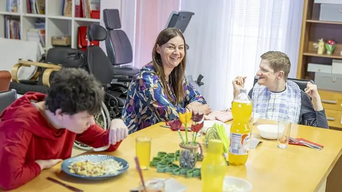 Drei Personen sitzen an einem gedeckten Tisch und essen gemeinsam