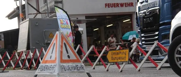 Ein Feuerwehr- und Umleitungsschild stehen auf dem Asphaltboden, dahinter die Feuerwehr