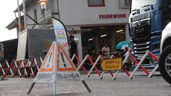 Ein Feuerwehr- und Umleitungsschild stehen auf dem Asphaltboden, dahinter die Feuerwehr